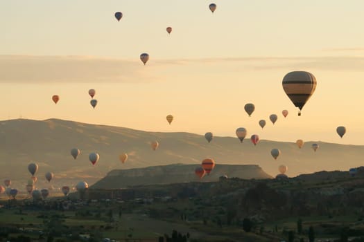 Colorful hot air balloons over the landscape of the Red Valley, Rose Valley about to land next to Cavusin after sunrise, Cappadocia, Turkey 2022
