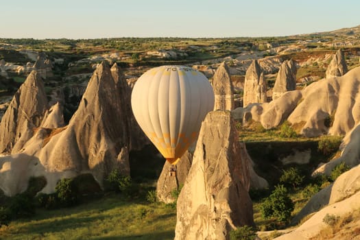 Yellow and white hot air balloon maneuvering between the fairy chimneys of Cappadocia, close to Göreme, Cappadocia, Turkey 2022