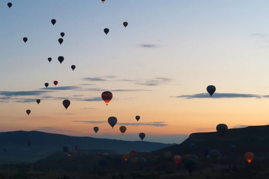 Many hot air balloons rising over the landscape of the Red Valley, Rose Valley before sunrise, close to Goreme, Cavusin, Cappadocia, Turkey 2022