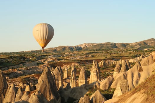 Yellow and white hot air balloon flying over the landscape of Cappadocia with its famous fairy chimneys, close to Göreme, Cappadocia, Turkey 2022