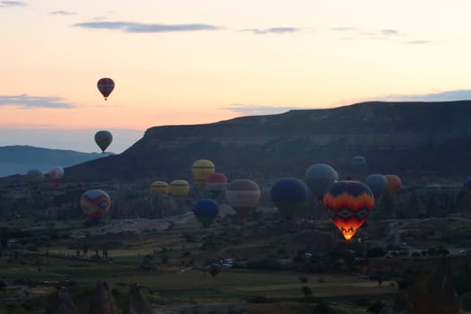 Hot air balloons rising from the balloon take off point next to Rose Valley, Red Valley in the early morning, close to Göreme, Cavusin, Cappadocia, Turkey 2022