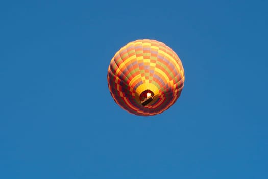 Shot of a colorful hot air balloon, taken from below in front of a bright blue morning sky, Göreme, Cappadocia, Turkey 2022