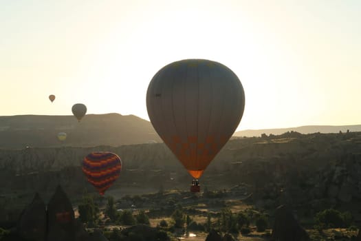 Several hot air balloons illuminated by the early morning sun while flying over the landscape of Cappadocia, close to Göreme, Cappadocia, Turkey