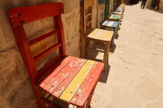 A row of colorful wooden chairs in a row in front of a wall in the old town of Mardin, Turkey 2022