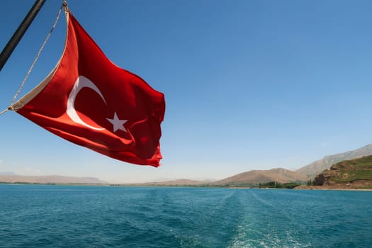 Red national flag of turkey flying, waving in the wind on the boat ride crossing Lake Van, Van Gölü to Akdamar Island, close to Van, Turkey 2022