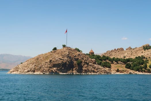 Akdamar Island on Lake Van, Van Gölü, seen from a boat, the turkish flag waving, flying on a pole and the top of the Armenian Cathedral of the Holy Cross are visible, Van, Turkey 2022