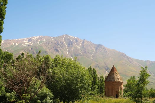 The Halime Hatun tomb, grave, mausoleum, Halime Hatun Kümbeti with the snow covered Mount Artos in the background and a little forest next to it, close to Lake Van, Van Gölü, Gevas, Turkey 2022