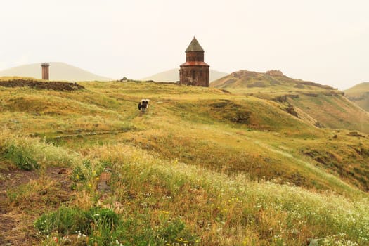 People walking to the Church of St., Saint Gregory of Abughamir, Abughamrens, Abughamrents on a rainy day with umbrellas, the Citadel and the Minaret of the Mosque of Minuchihr can be seen in the background, ancient armenian city of Ani, Kars, Turkey 2022