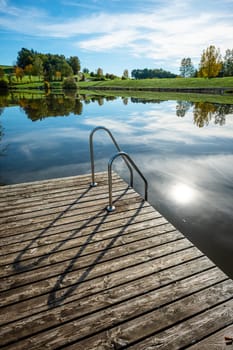 Dock at a lake with back lit sun and green meadow scenery