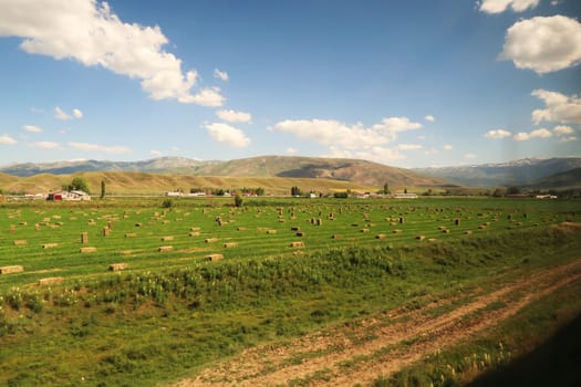 Passing farming, agriculture on the train ride in the Eastern Express, Dogu Ekspresi from Kars to Ankara, green field with hay bales on it, Turkey 2022
