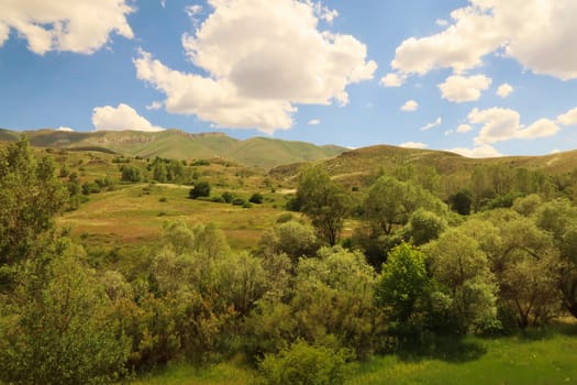 Beautiful landscape seen on the train ride in the Eastern Express, Dogu Ekspresi from Kars to Ankara, hills, mountains, meadows, fields and forest in front of a blue sky with clouds, Turkey 2022
