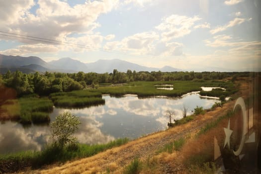 Beautiful landscape seen on the train ride in the Eastern Express, Dogu Ekspresi from Kars to Ankara, reflection of clouds in a pond, swamp surrounded by forest, mountains in the background, Turkey 2022