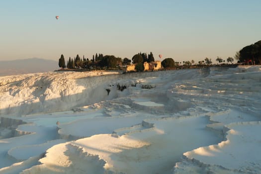 The travertines of Pamukkale early in the morning with hot air balloons rising in the back, Denizli, Turkey 2022