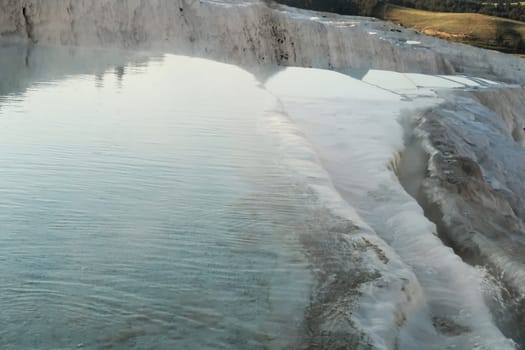 Intense blue and steaming water running over the layers of travertine terraces at Pamukkale in the early morning, Denizli, Turkey 2022
