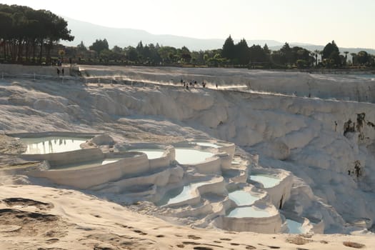 A few people walking up the travertine terraces in Pamukkale in the early morning, steam coming up from the hot water, Denizli, Turkey 2022