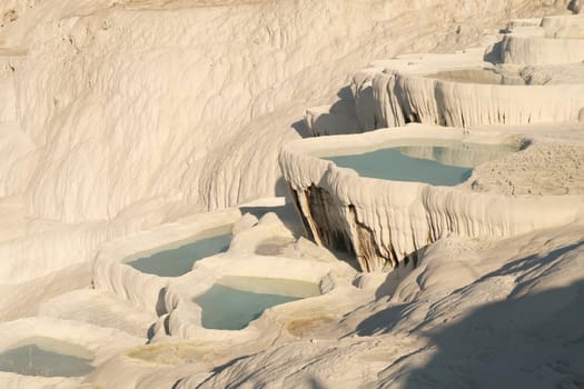 The sun shining onto the travertine terraces of Pamukkale, filled with intense blue water, Denizli Turkey 2022