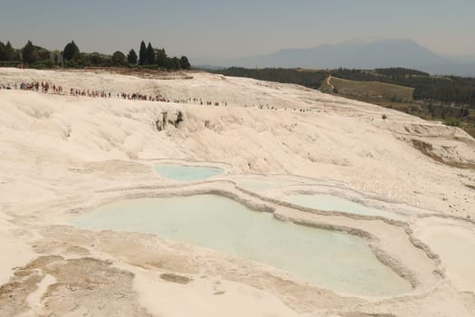A crowd of people climbing up the travertine pools in Pamukkale from the lower gate on a busy day, Denizli, Turkey 2022