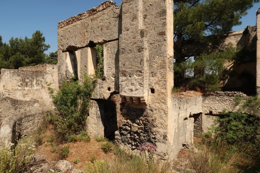 Leftover exterior wall of one of the houses in the abandoned village of Kayaköy with chimney, windows and garden, near Fethiye, Turkey