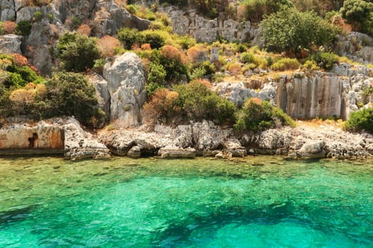 Submerged foundation in the foreground and structures and wall with window and doors onshore in the background at the ancient sunken city of Kekova, Kekova Island, Demre, Turkey 2022