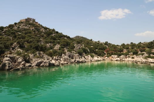 The green water in the Burc Koyu Bay, a roman castle can be seen on a hilltop on the left, close to Demre, Turkey 2022