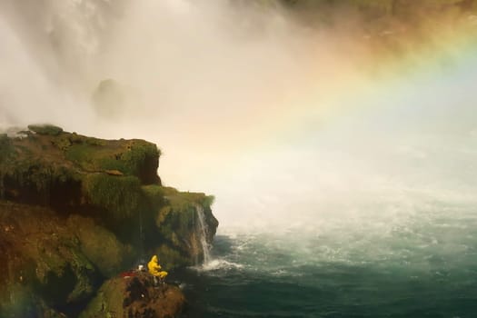 Fisherman in bright yellow raincoat fishing from a rock right next to the Düden Waterfalls in Antalya, Turkey 2022