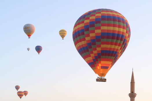 Colorful group of air balloons in the early morning over the town of Göreme with the tower of a Minaret right next to it, Göreme, Cappadocia, Turkey 2022
