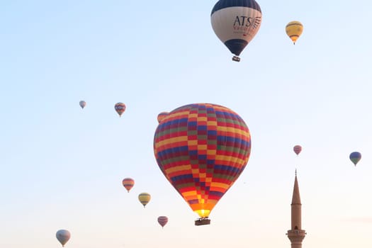 Hot air balloons in the early morning over the town of Göreme with the tower of a Minaret right next to it, Göreme, Cappadocia, Turkey 2022