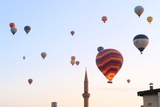Colorful hot air balloons in the early morning over the town of Göreme with the tower of a Minaret right next to it, Göreme, Cappadocia, Turkey 2022