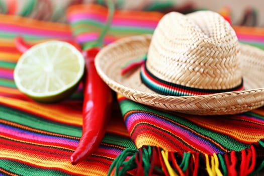 A Mexican sombrero rests on a colorful serape with a lime and chili pepper, invoking festive Cinco de Mayo vibes.