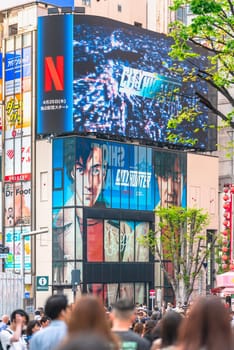 tokyo, japan - apr 28 2024: Crowd walking towards the poster of the Netflix movie "City Hunter"" or ""Nicky Larson"" under the movie trailer displayed on a curved screen at the exit of Shinjuku Station."