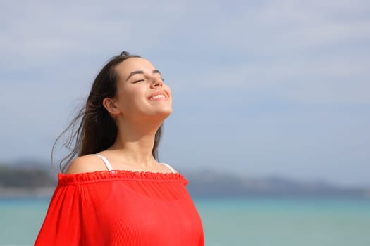 Happy woman in red breathing fresh air and smiling on the beach