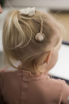 Funny baby with cochlear implant sitting at home and eating. Hear aid and medicine innovating technology and diversity concept