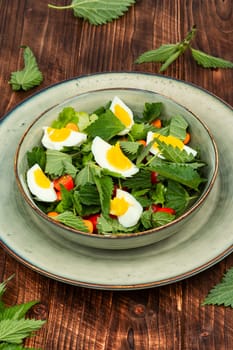 Bowl with healthy salad of nettle leaves, eggs and tomatoes on rustic wooden table.