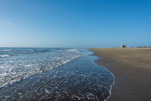 Sandy beach by the sea with waves and blue sky,Sandy beach by the sea with waves and blue sky