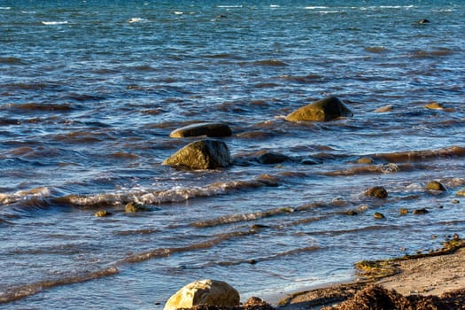 Big stones lie in the water on the Baltic Sea coast, with waves