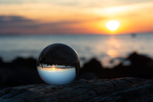 Glass ball on a branch at sunset on the beach, the sea and the setting sun are reflected in the ball