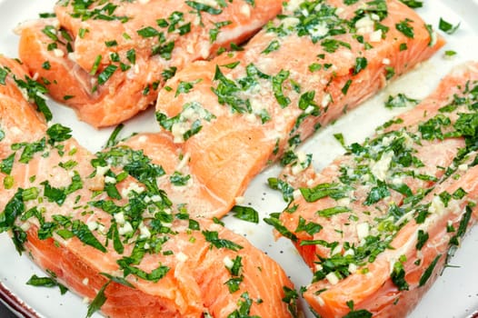 Fresh raw salmon fillet fish in garlic herbs marinade ready for baking. Close up.