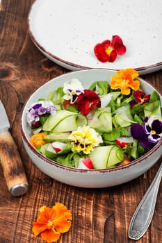 Healthy salad made from fresh vegetables and decorated with edible flowers on rustic wooden table.