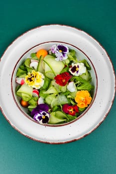 Healthy salad made from fresh vegetables and decorated with edible flowers on rustic wooden table.