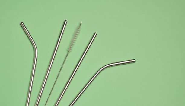 Metal straws for cocktails and a cleaning brush on a green background, top view