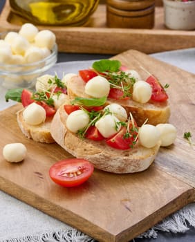Round mozzarella, cherry tomatoes and microgreens on a piece of white bread, a healthy sandwich