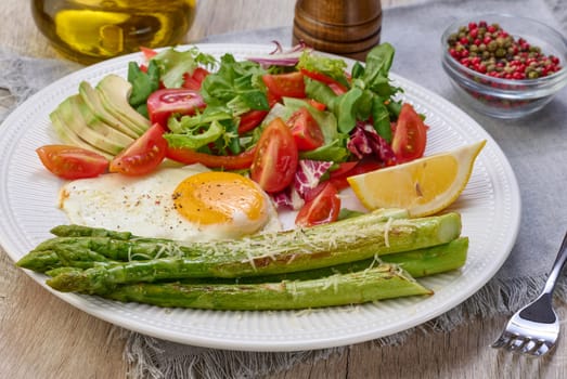 Round plate with cooked asparagus, fried egg, avocado and fresh vegetable salad on the table, top view