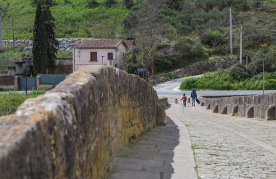 Mother and daughter crossing the Romanesque bridge of Puente La Reina, Navarre, Spain