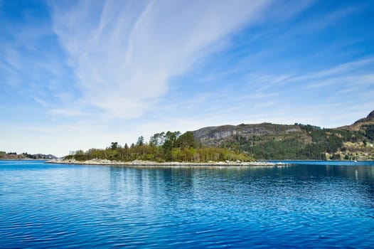 Island with rocks and trees in the fjord in front of the open sea in Norway. The water glistens in the sun. Landscape from the north