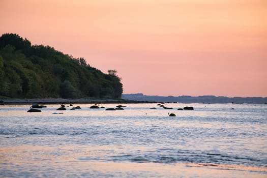 Sunset, illuminated sea. Sandy beach in the foreground. Light waves. Poel island on the Baltic Sea. Nature photo from the coast
