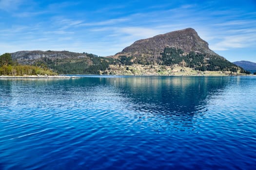 Island with rocks and trees in the fjord in front of the open sea in Norway. The water glistens in the sun. Landscape from the north