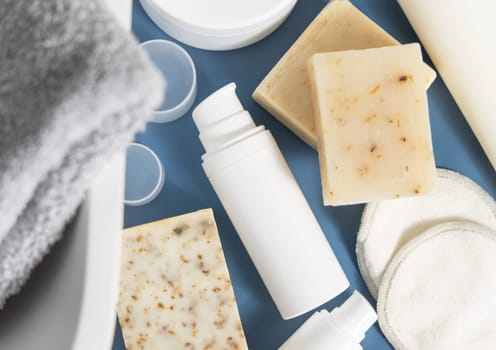 White one pump cosmetic bottle near soap bars and basin on blue countertop in bathroom top view, mockup. Modern lifestile scene with female personal care and beauty products
