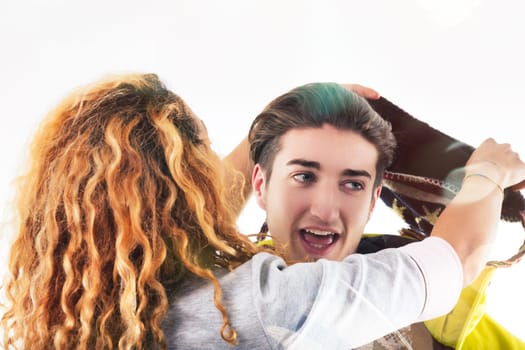 young woman in a yellow jacket laughs heartily as she adjusts a festive hat on her male friend's head
