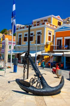 SYMI, Greece - 03 JUNE 2021. A old big Anchor sculpture on Symi town promenade on the pictorial port of Symi island in Greece. Dodecanese.