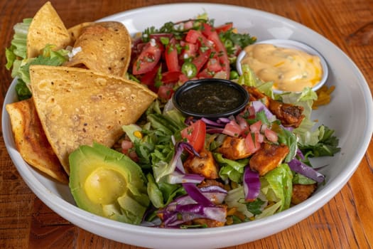 A white bowl brimming with a vibrant salad next to crunchy tortilla chips, creating a playful and colorful food composition.